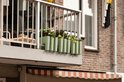Olijfgroene balkonplantenbak met 5 vakken, gedecoreerd met bloemen, hangend aan een balkonreling.