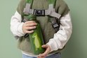 Groene drinkfles met witte stippen en een lichtgroene krokodil. Een jongen met rugzak houdt hem vast.