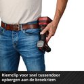 Een man met spijkerbroek en riem, die een rode en zwarte boormachine in zijn broekzak doet met de riemclip.