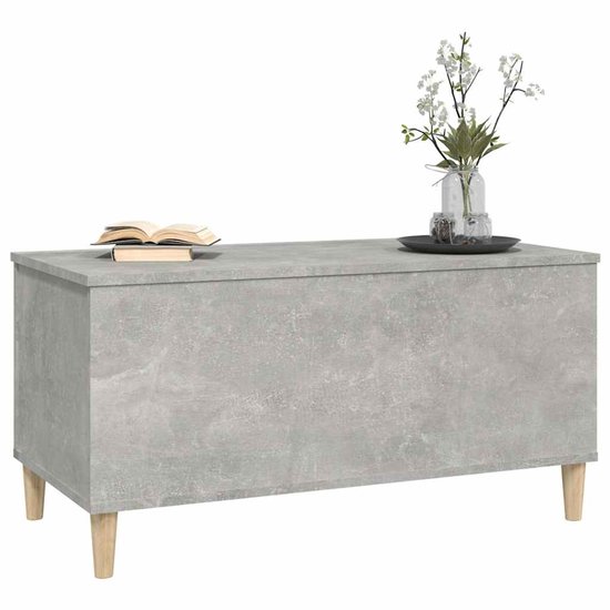 Betongrijze salontafel met een gesloten blad, met een boek en vaas erop, en houten pootjes.