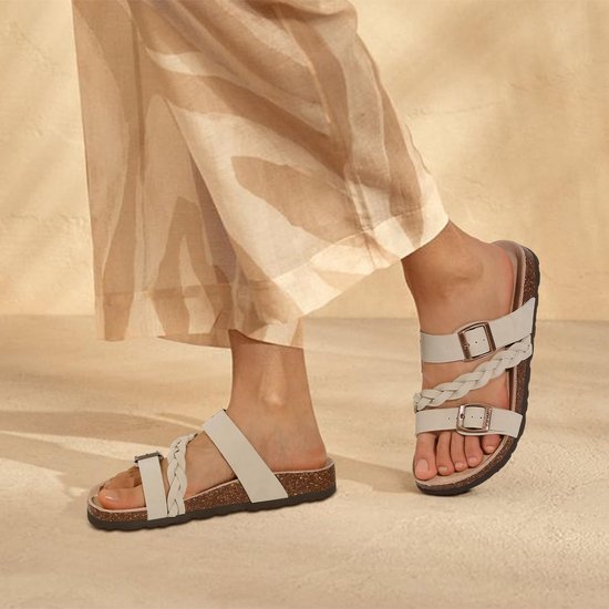 Voeten van een model dat beige sandalen met gevlochten bandjes en gespen draagt.
