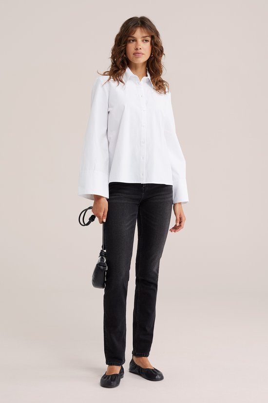 Model met bruin haar draagt zwarte slim fit jeans en een oversized witte blouse.