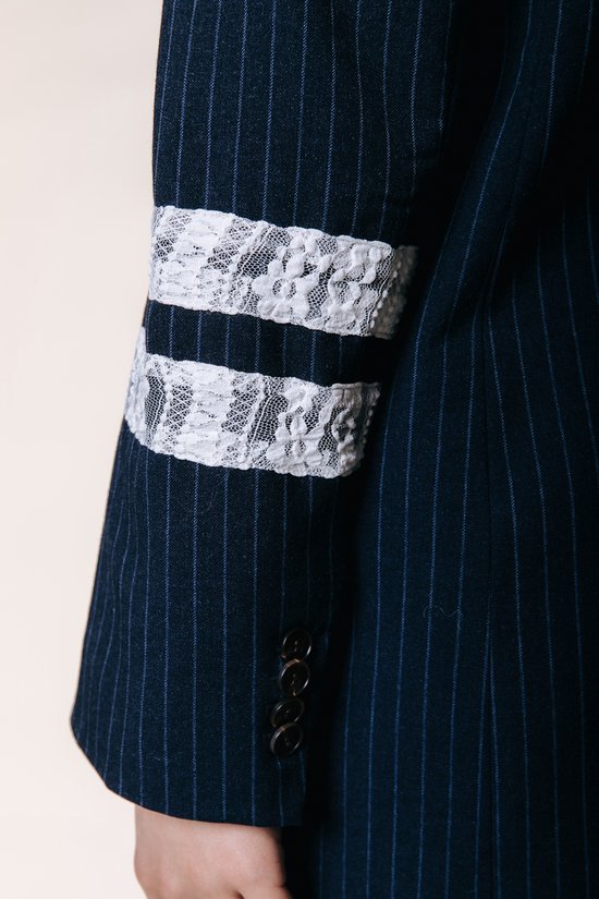 Detail van de donkerblauwe krijtstreepp blazer met twee witte kanten banden op de mouw.
