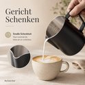 Zwarte RVS melkkan van 600ml met smalle schenktuit, die melk schenkt in een mok voor latte art. Met maatverdeling in ml en oz.