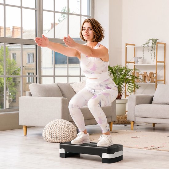 Vrouw in sportkleding met print doet een squat op een zwarte step met witte en grijze accenten.