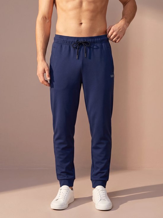 Donkerblauwe sportbroek met trekkoord en logo op de zijkant, gedragen door een man.