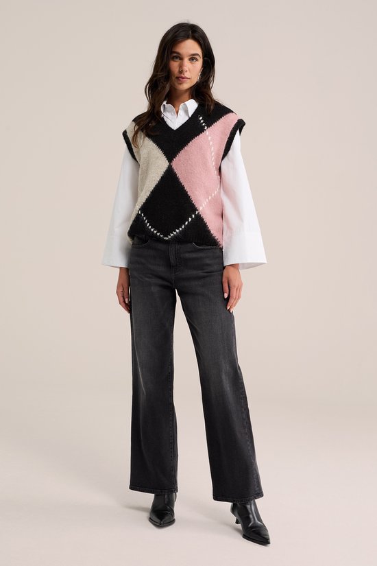 Model draagt een gebreide spencer met ruitpatroon in roze, zwart en beige, met witte blouse en jeans.