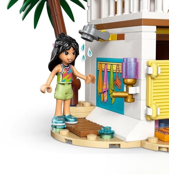 Meisje met donkere staartjes bij de buitendouche van een LEGO strandhuis. Ze draagt een groen topje en lichtgroene short.