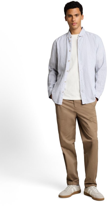 Man met beige chino, wit T-shirt en gestreept linnen overhemd met open knopen.