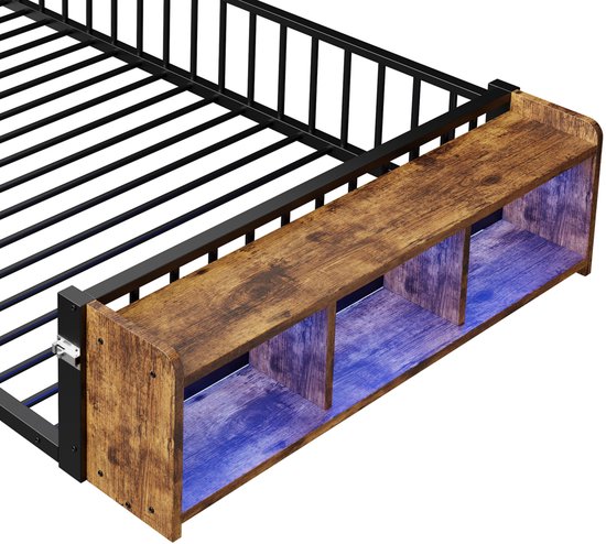 Detail van een zwart metalen kinderbed met houten opbergvak en roze LED-verlichting aan het hoofdeinde.