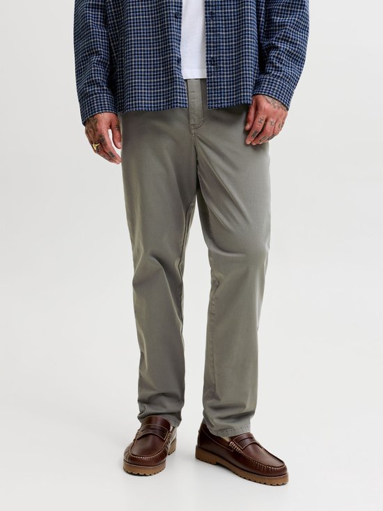 Man met grijze chino, wit T-shirt en blauw geruit overhemd, draagt bruine loafers.