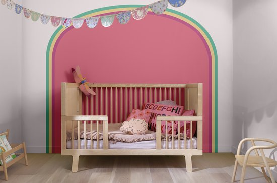 Een houten ledikantje met Barbie-thema, versierd met roze kussens en een slinger. Roze boog op de muur.