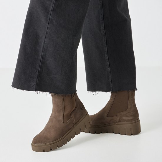 Bruine suède chelsea boots met dikke zool, gedragen door model met zwarte jeans.