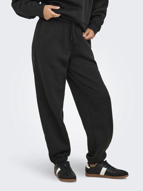 Een vrouw draagt een zwarte joggingbroek met trekkoord, elastische enkelbanden en sneakers met witte strepen.