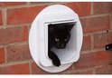 Zwarte kat komt door een wit kattenluik in een bakstenen muur.