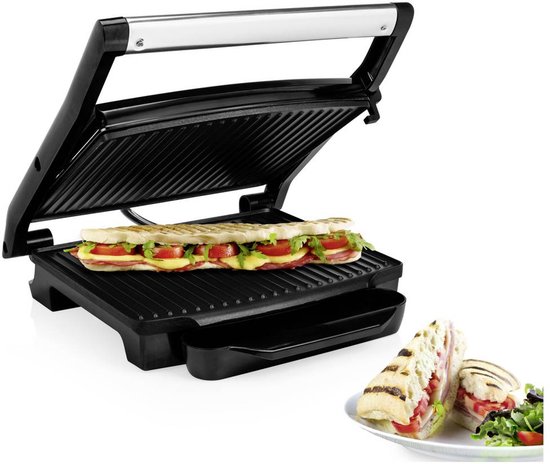 Open zwarte grill met een lange panini in, gevuld met brood, kaas, tomaat en sla. Een halve panini op een bord ernaast.