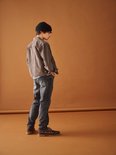 Jongen met zwarte muts, bruine jas en grijze jeans.
