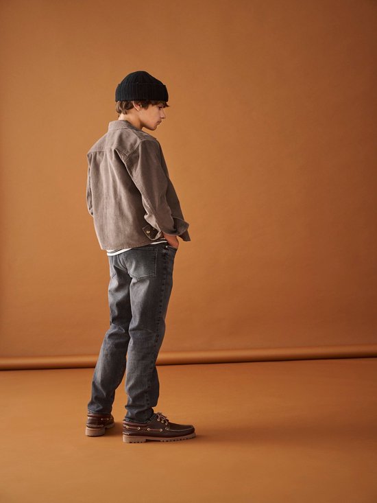 Jongen met zwarte muts, bruine jas en grijze jeans.
