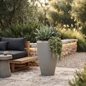 Un grand vase gris conique à la finition texturée, placé à l'extérieur avec une plante d'agave et des succulentes.