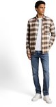 Man met een witte longsleeve en een bruin geruite blouse, met een blauwe jeans.