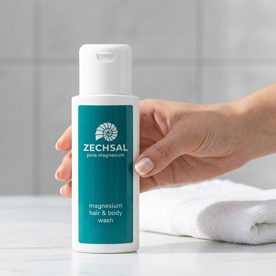 Een hand houdt een witte fles Zechsal magnesium haar & body wash vast met een groen label.
