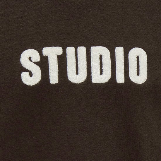 Close-up van witte 'STUDIO' letters op een bruine sweater.