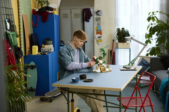 Jonge man bouwt aan een groene LEGO Rayquaza bovenop een bruin stenen altaar met witte wolkjes.