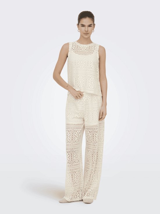 Model draagt een crèmewitte tweedelige kanten set met wijde broek en mouwloze top.