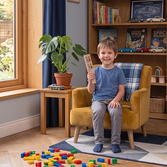 Jongetje zit lachend op gele fauteuil met houten tamboerijn.