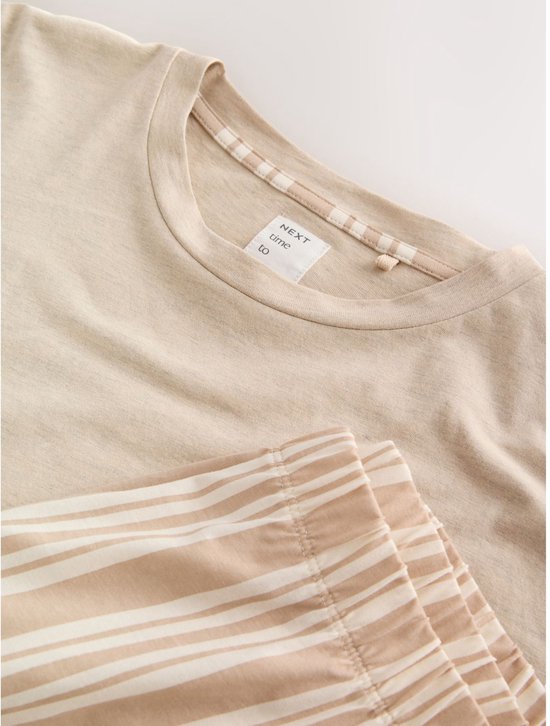 Close-up van de neklijn van een beige T-shirt en de tailleband van een short met verticale strepen.