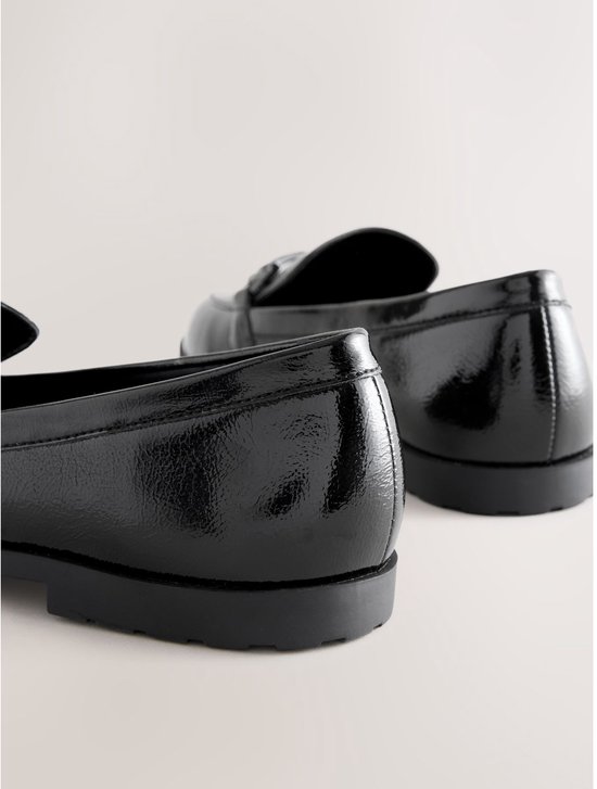 Achterkant van zwarte glanzende loafers met zilverkleurige gespen.