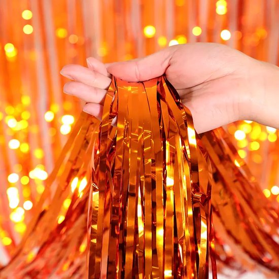 Oranje glitterfranjes die vastgehouden worden door een hand, met bokeh-lichtjes op de achtergrond.