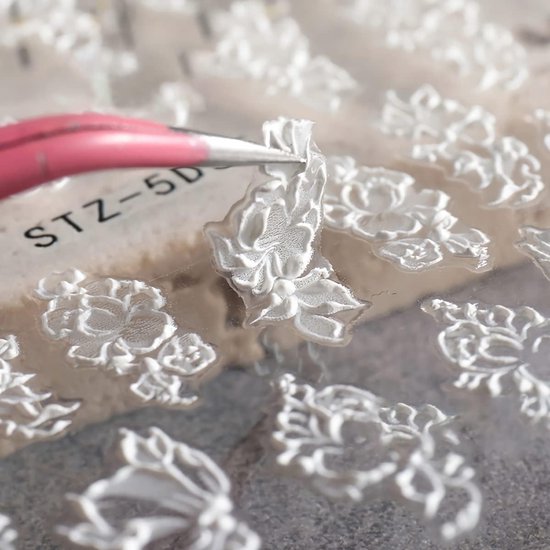Gedetailleerde close-up van witte 3D-bloem nagelstickers met een pincet.