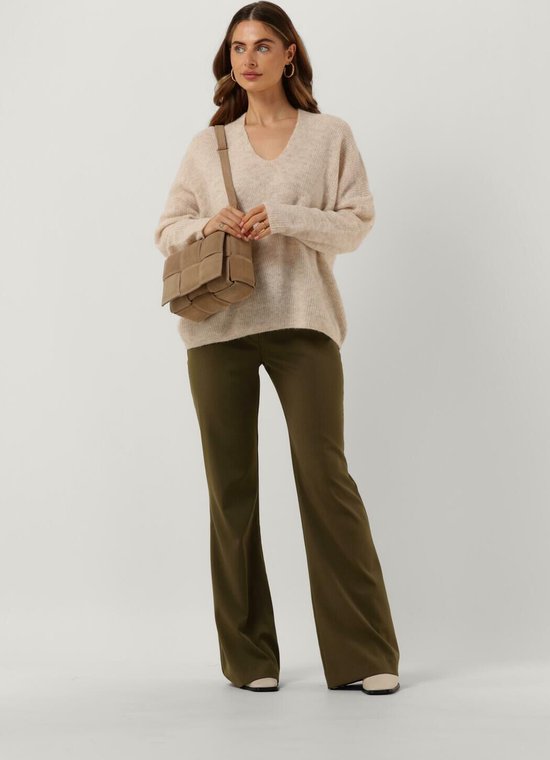 Model draagt een beige gebreide trui en een donkergroene pantalon met wijde pijpen. Ze draagt een beige schoudertas.