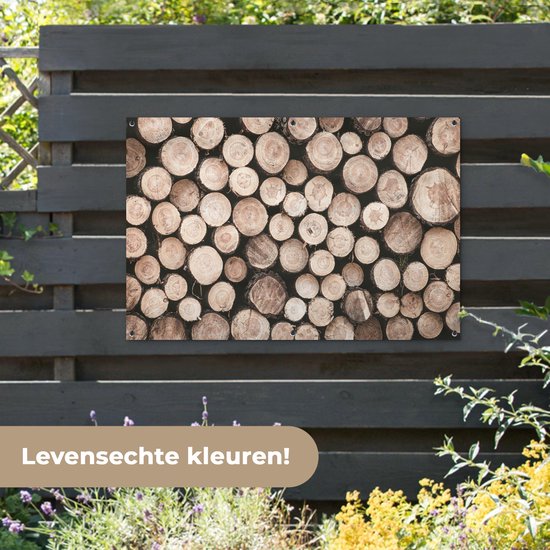Une affiche avec des bûches empilées, de différents diamètres et teintes naturelles, accrochée à une clôture gris foncé.
