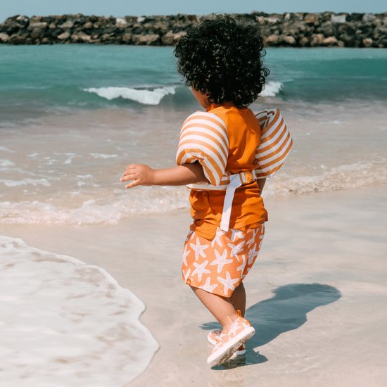 Kind met zwembandjes met oranje-witte strepen en zwembroek met zeesterren.