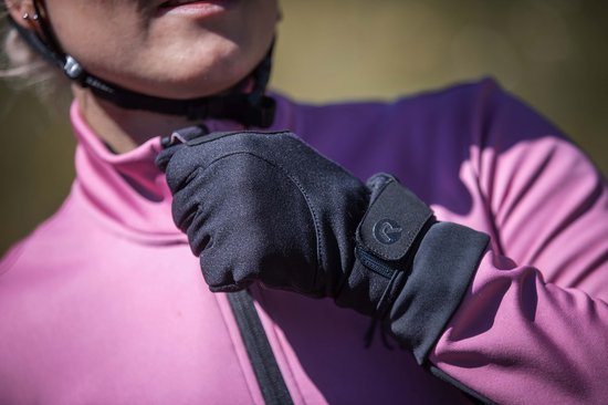 Een persoon met een roze jack en zwarte Rogelli winter fietshandschoenen met klittenbandsluiting.