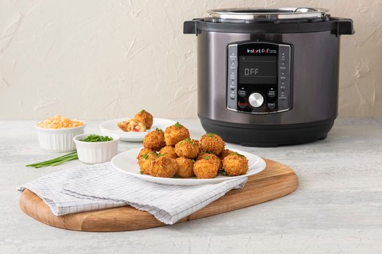 Een Instant Pot multicooker met een stapel gefrituurde hapjes op een wit bord, naast schaaltjes met geraspte kaas en bieslook.