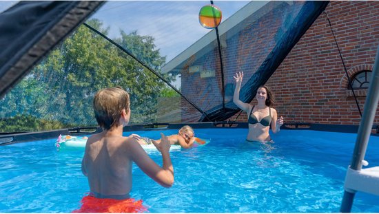 Volwassenen en kinderen spelen in een zwembad onder een koepel, gooien met een bal.