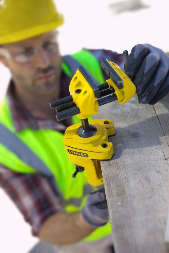 Gele multifunctionele boorklem van Stanley met gele en groene werkkleding, bevestigd aan hout.