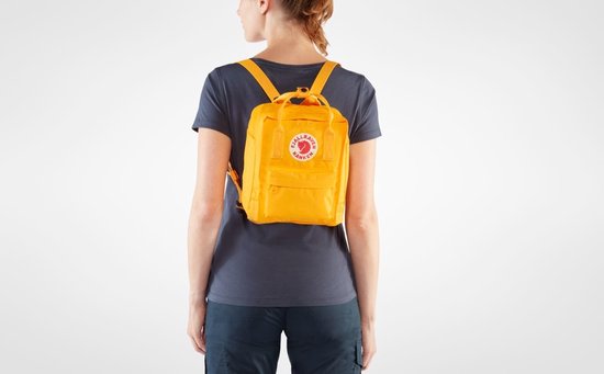 Vrouw draagt een gele Kånken rugzak op haar rug.