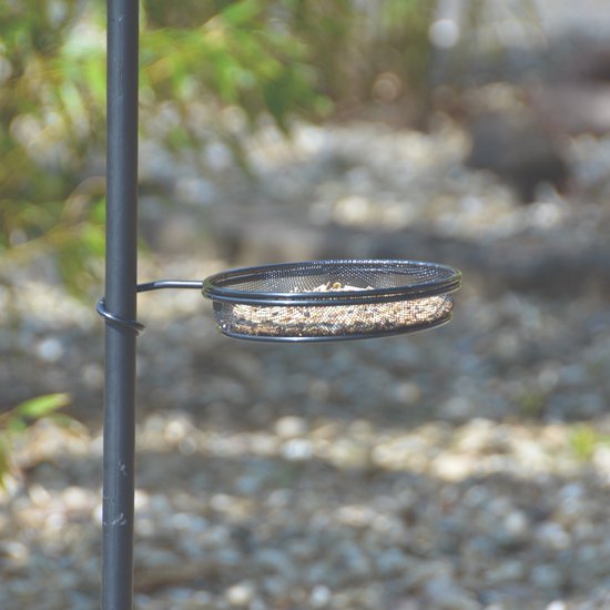 Detail van een zwart vogelvoederbakje gevuld met vogelvoer.