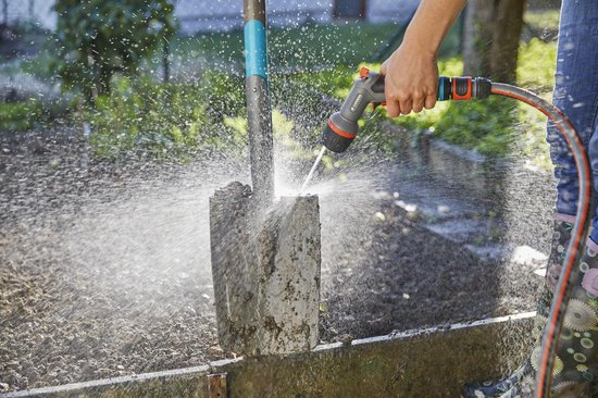 Persoon met GARDENA Comfort EcoPulse spuitpistool sproeit modder van een spade af.