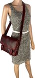 Sac bandoulière en cuir rouge porté par une mannequin avec une robe grise abstraite.