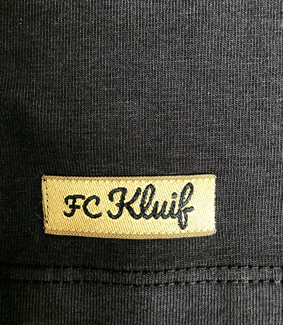 Gouden label met zwarte tekst 'FC Kluif' op een zwart textiel.