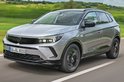 Grijze Opel Grandland SUV rijdt op een weg, voorkant zichtbaar.