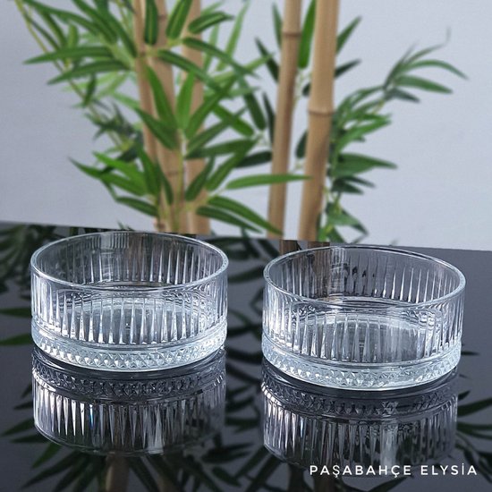 Twee glazen, cilindervormige tapasschaaltjes met verticale ribbels en een gedetailleerde bodem, met weerspiegeling.