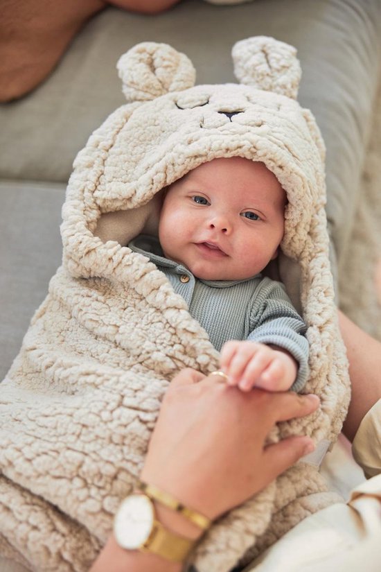 Crèmekleurige teddy wikkeldeken met konijnenoren en gezichtje, om een baby in een draagzak gewikkeld.