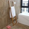 Houten ladderrek met een witte handdoek, tegen een muur met bruine tegels, naast een bad.