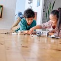 Twee kinderen leggen LEGO Ruimtevaart onderdelen uit. Een jongen met een groene trui en een meisje met een roze trui.